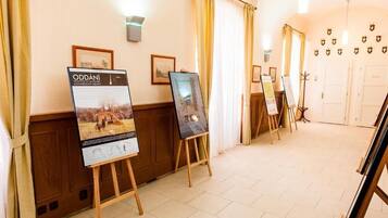 A hotel corridor with framed pictures on the walls, easels with paintings, and a wooden floor.