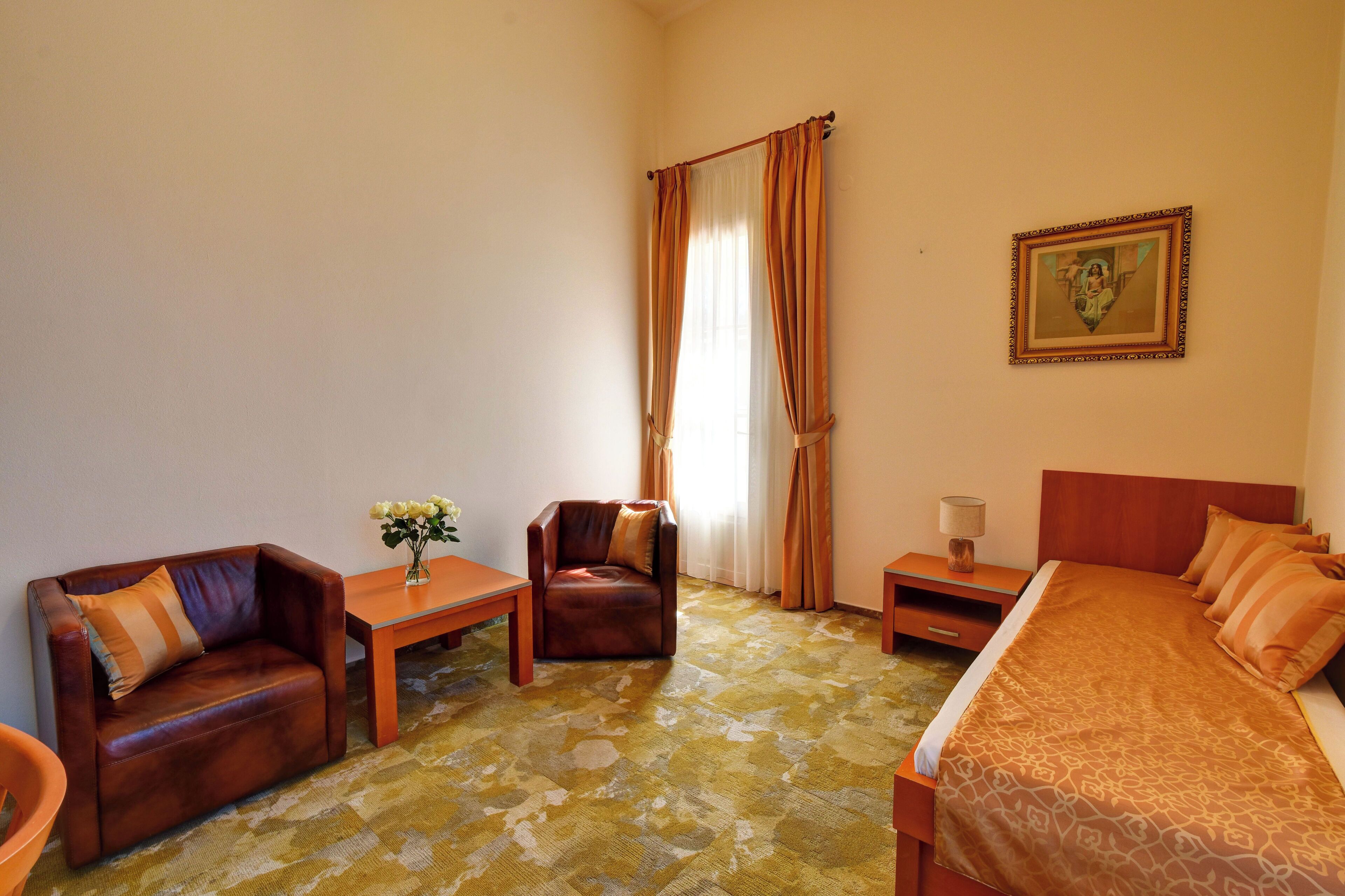 Ein Hotelzimmer mit einem Bett, einem Sofa, einem Sessel, einem kleinen Tisch mit Blumen und einem Nachttisch mit einer Lampe.