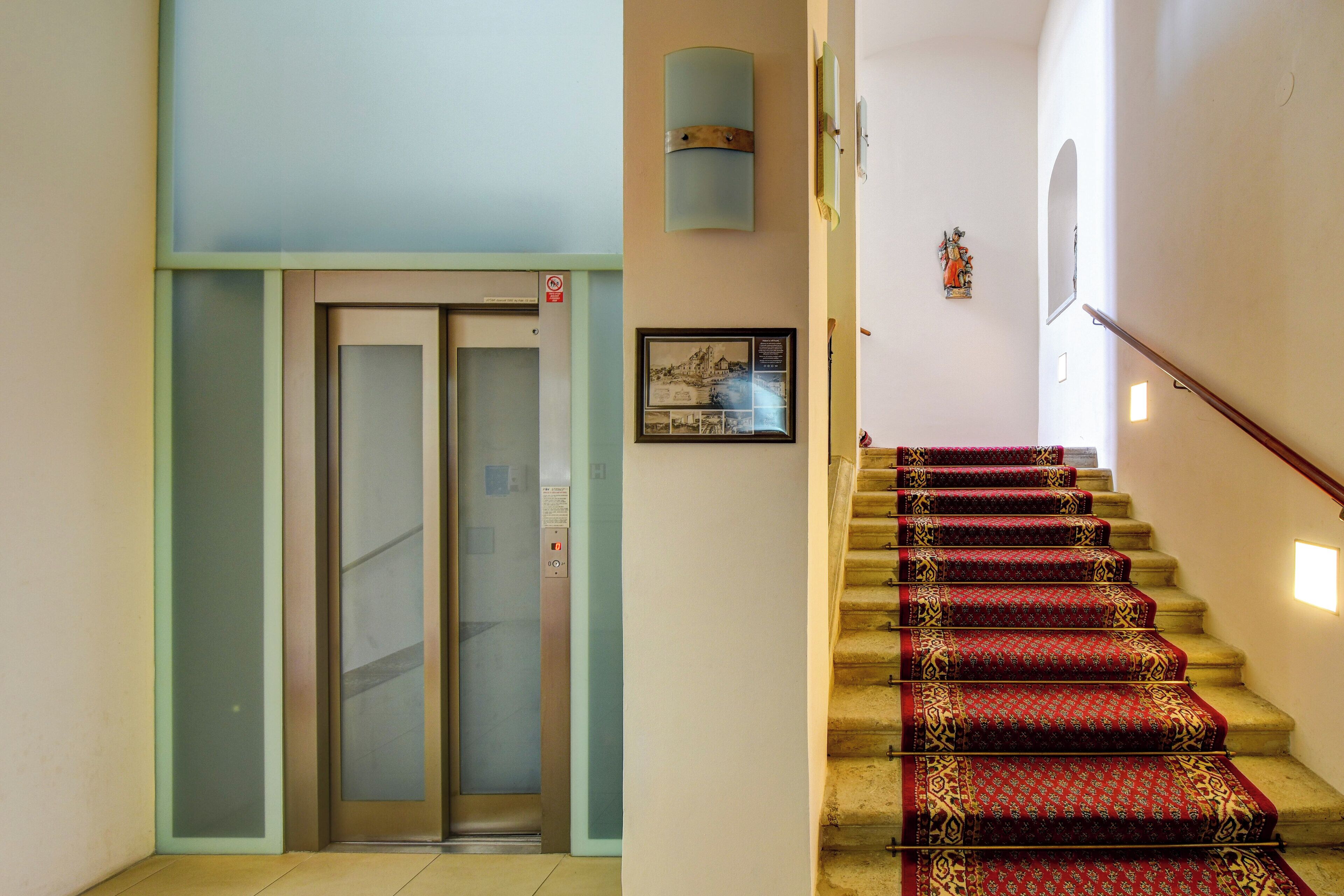 A staircase with red carpeted steps leading to an elevator.