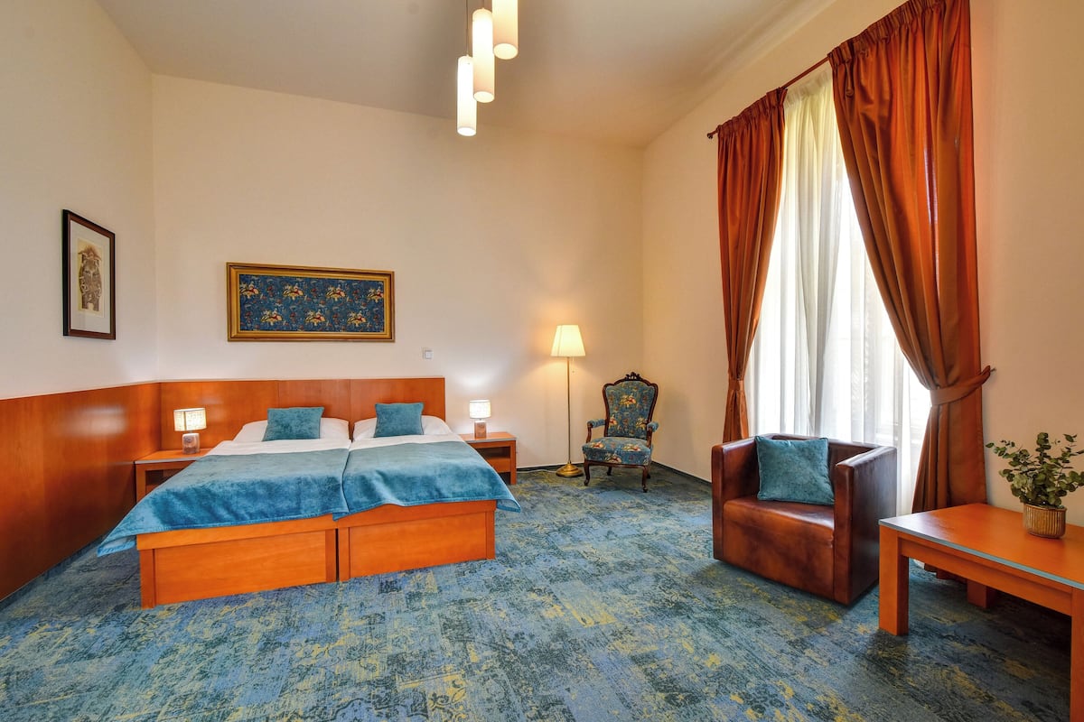 A hotel room with a large bed, a chair, a small table, and a lamp.