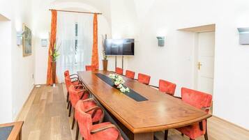Una sala de conferències amb una taula de fusta llarga, cadires vermelles, una televisió a la paret i una porta amb una creu.