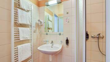 A bathroom with a white sink, a glass shelf, a towel rack, a mirror, and a shower.