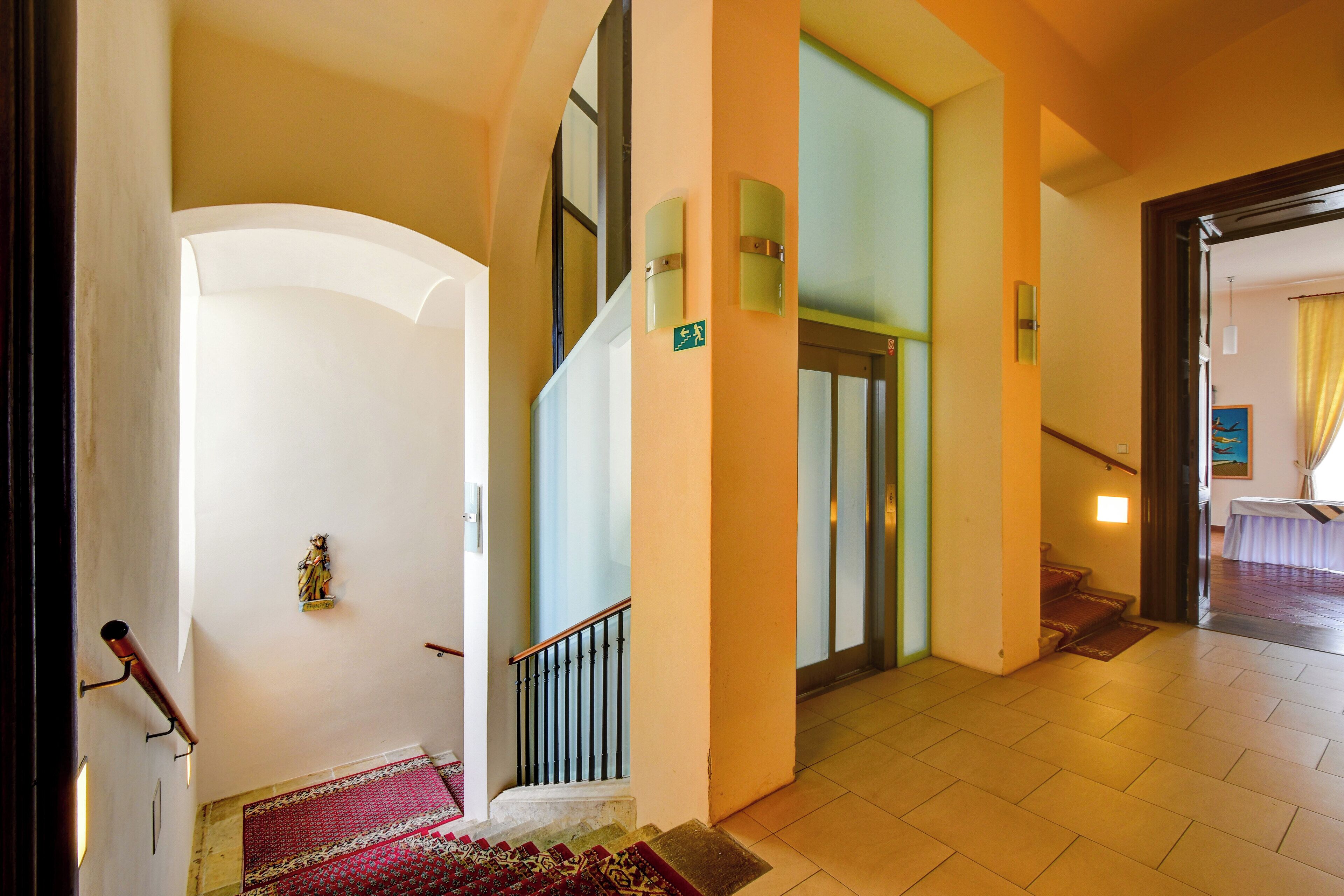 Un vestíbulo de hotel con una escalera, una recepción y vistas de la habitación contigua.