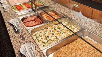 Un bufé con diferentes opciones de comida, como salchichas, huevos y tortillas.