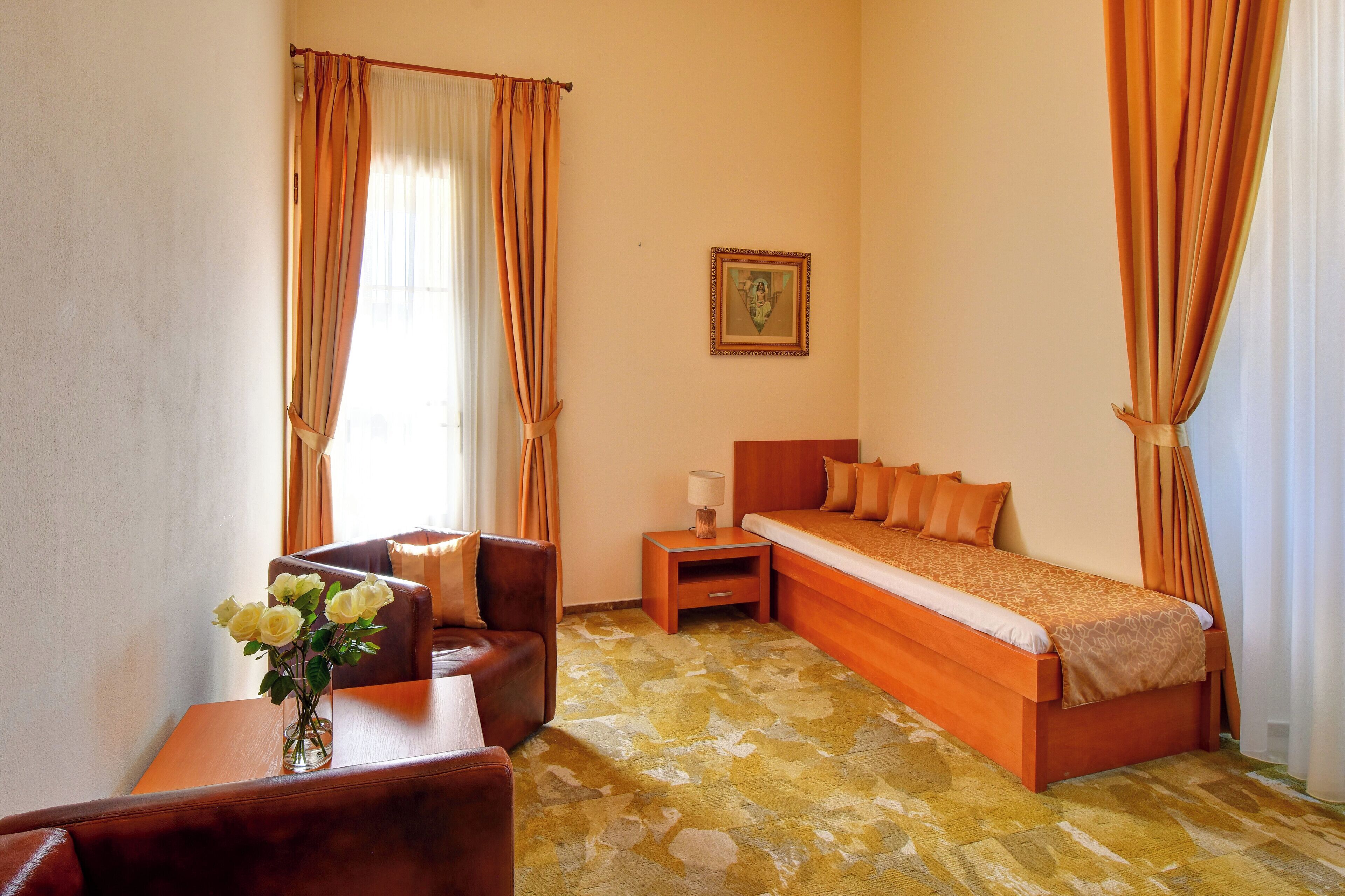 Una habitación de hotel con una cama, una silla, una mesita con un florero y una mesita de noche con una lámpara.