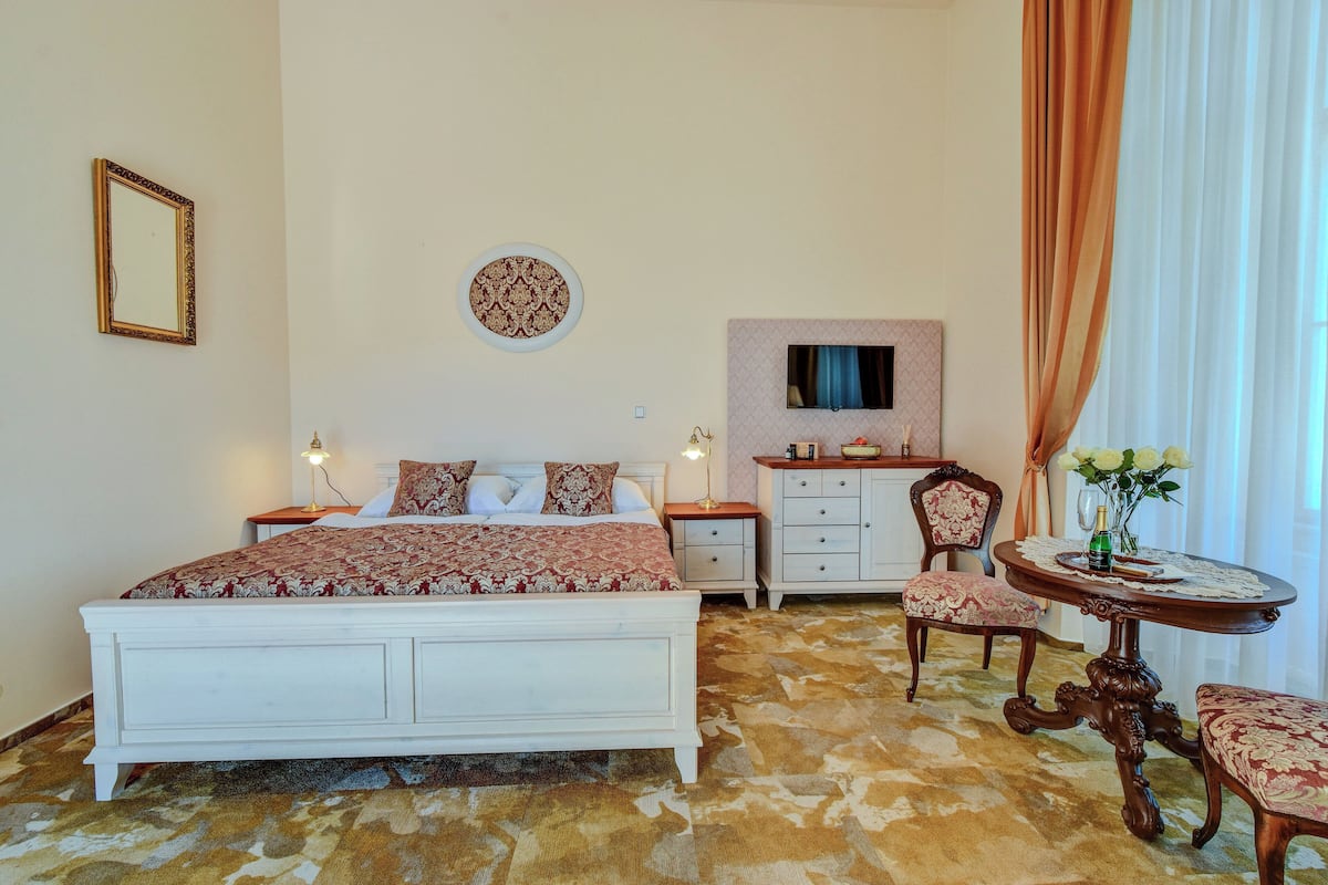 A bedroom with a bed, bedside tables, a dresser, a chair, and a small round table with a vase of flowers.