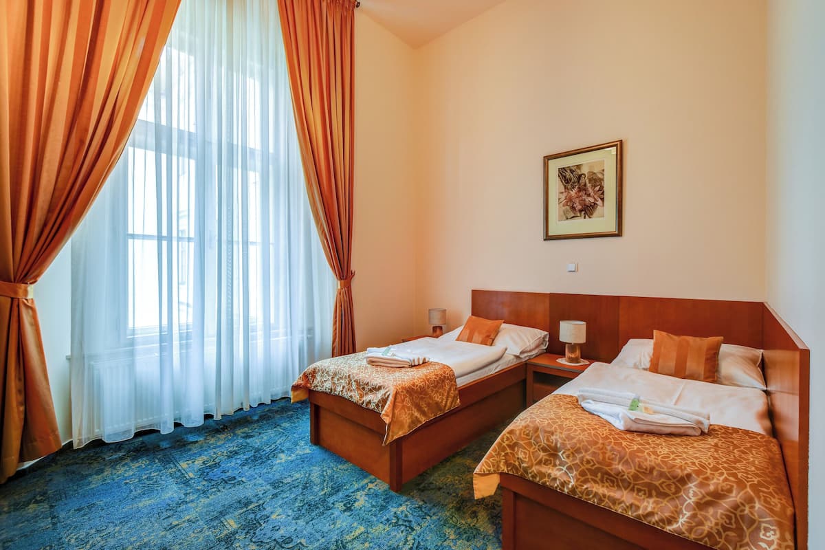 A hotel room with two beds, a large window with curtains, a framed picture on the wall, and a blue carpet.