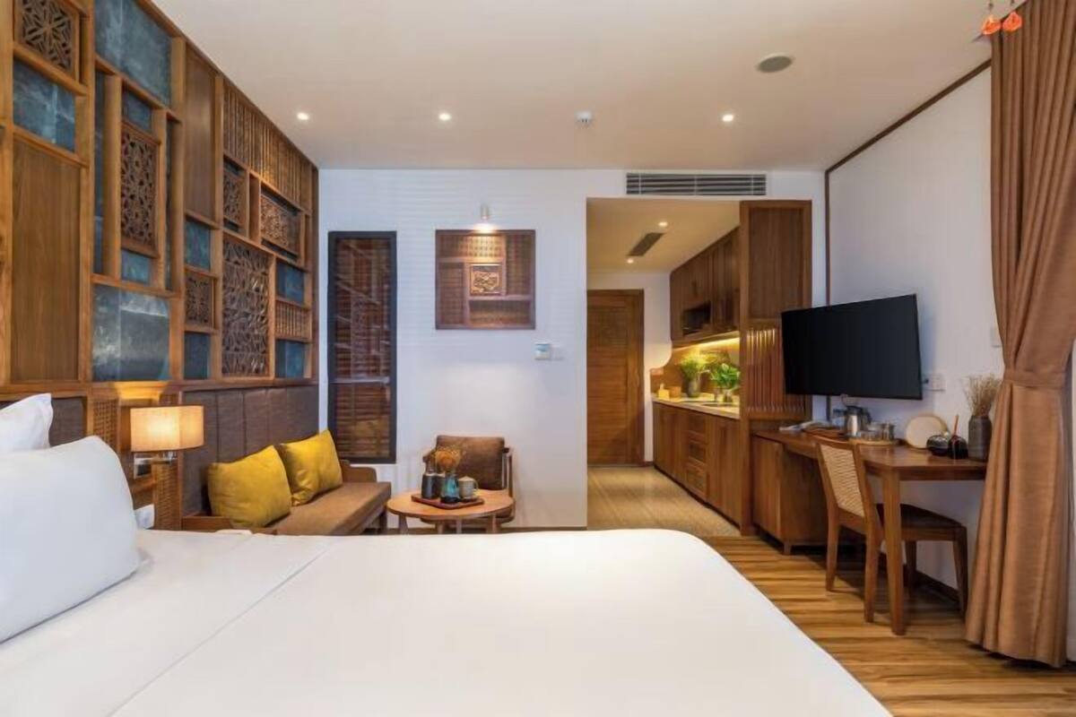 A hotel room with a bed, a sofa, a desk, a television, and a kitchen area.