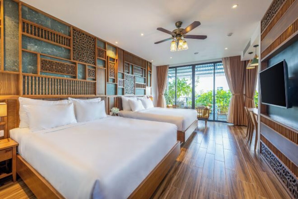 A hotel room with two beds, a ceiling fan, a TV, and a large window with a view of greenery.