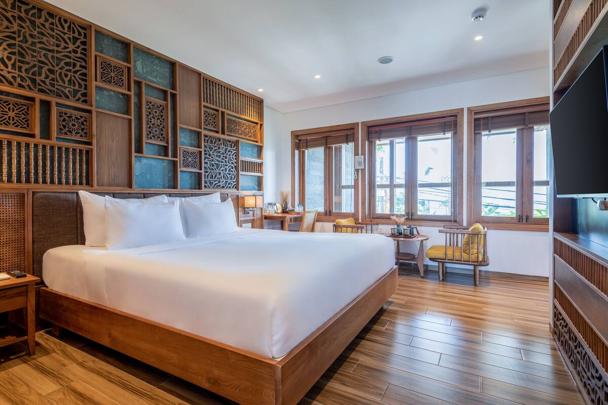 A spacious bedroom with a large bed, wooden flooring, a TV, and a decorative wall panel.