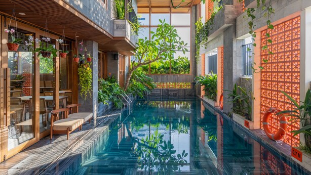 An indoor swimming pool with a wooden deck, surrounded by potted plants and a glass wall. - Bonny Boutique Hotel Da Nang (Da Nang)