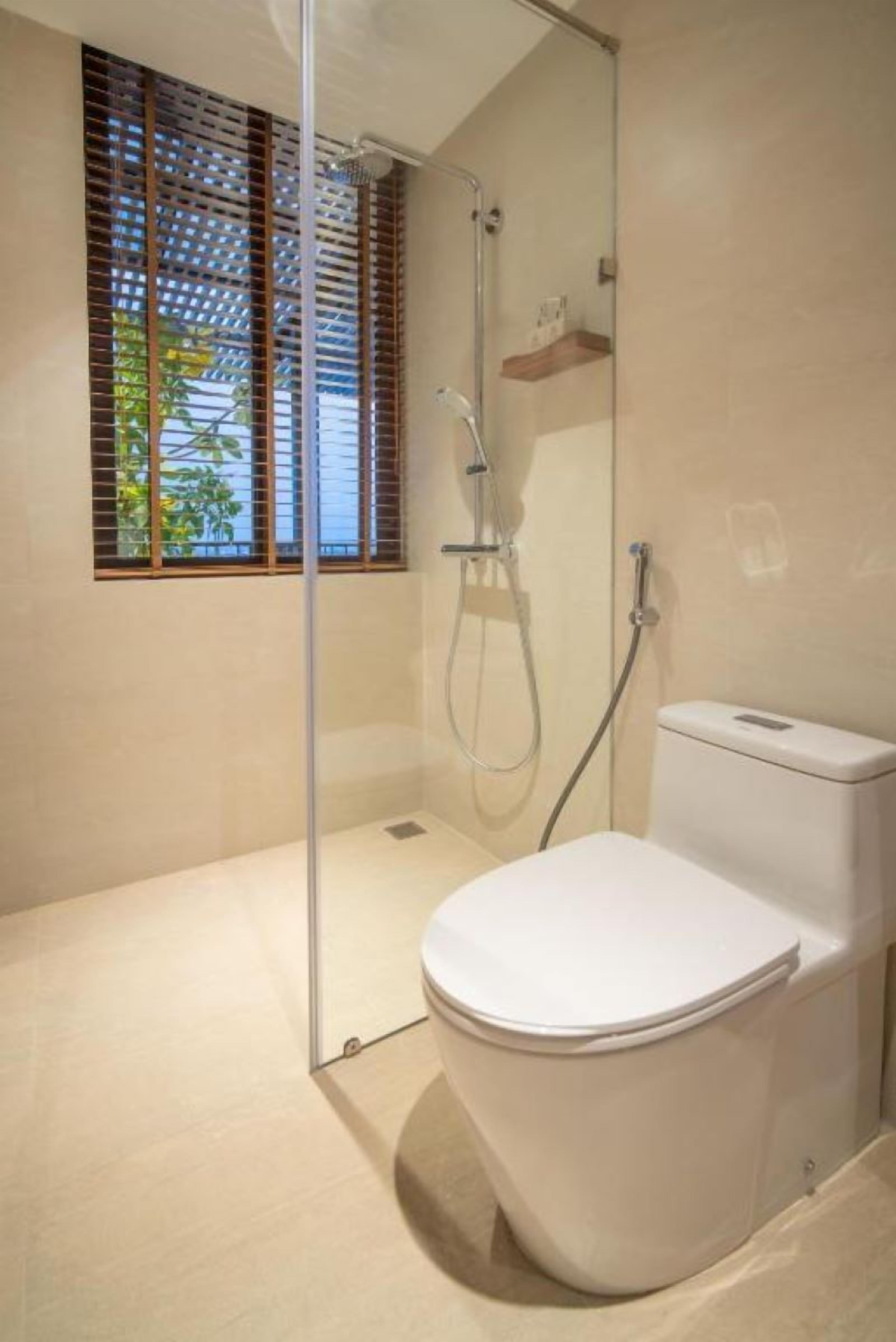 A modern bathroom with a glass-enclosed shower, a toilet, and a window with wooden blinds.