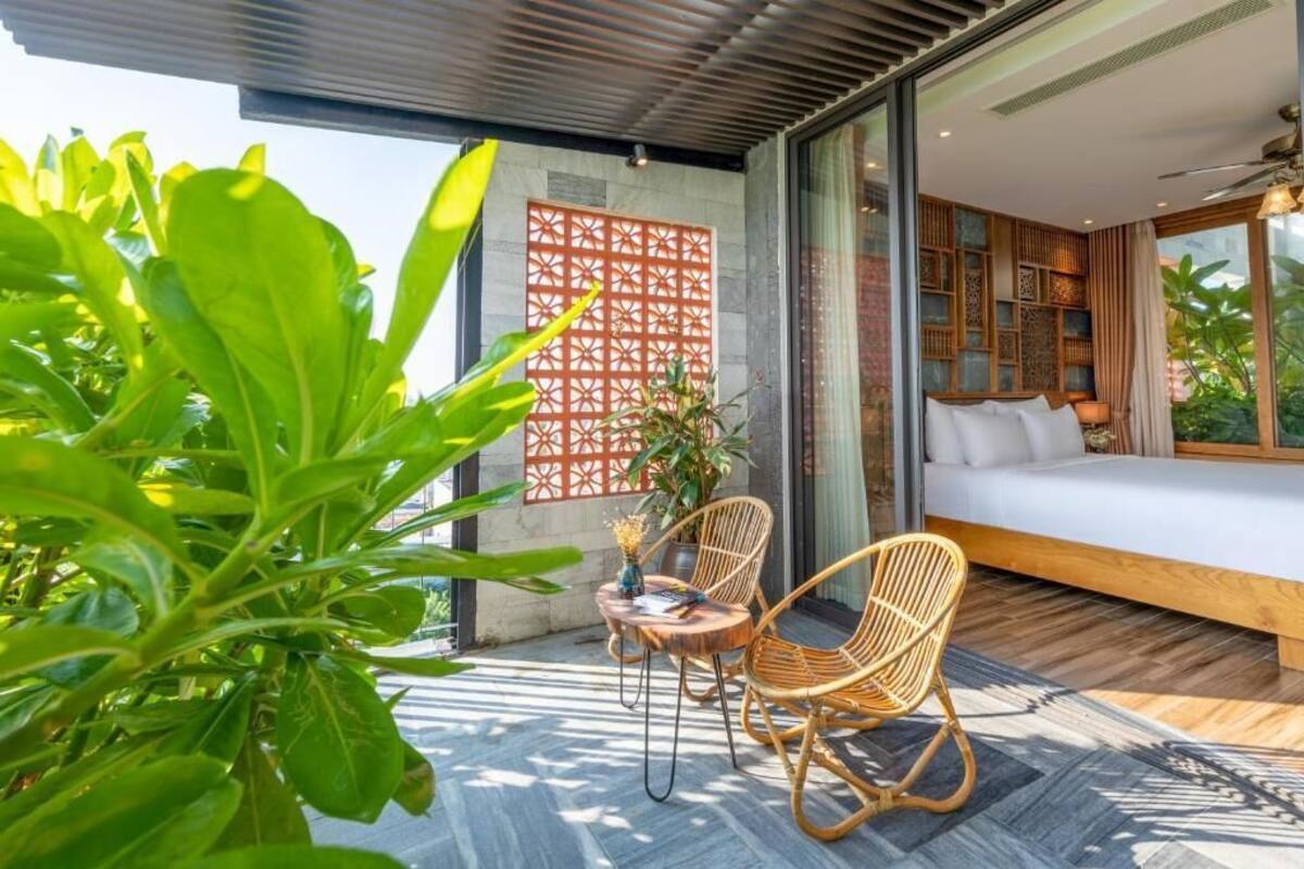 A modern bedroom with a large bed, a seating area with wicker chairs, and a view of greenery.