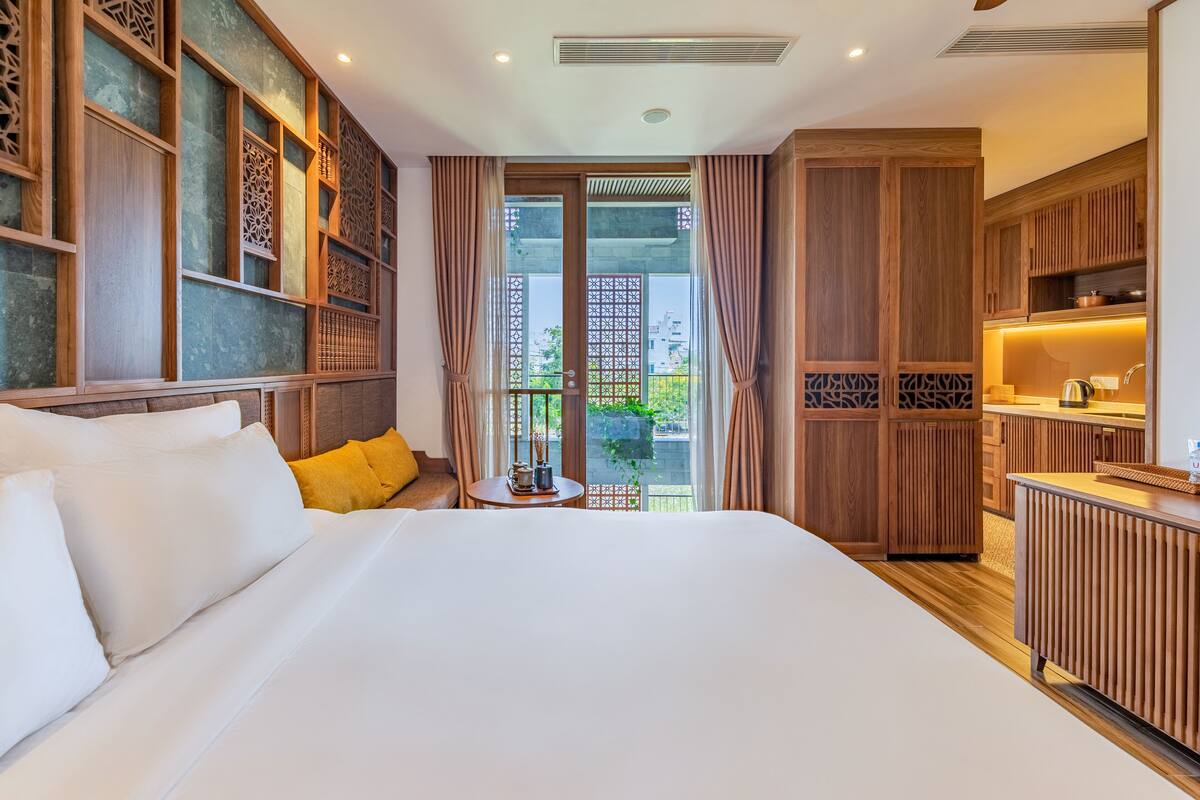 A hotel room with a large bed, wooden cabinets, a small table with a tea set, and a view of the outdoors.