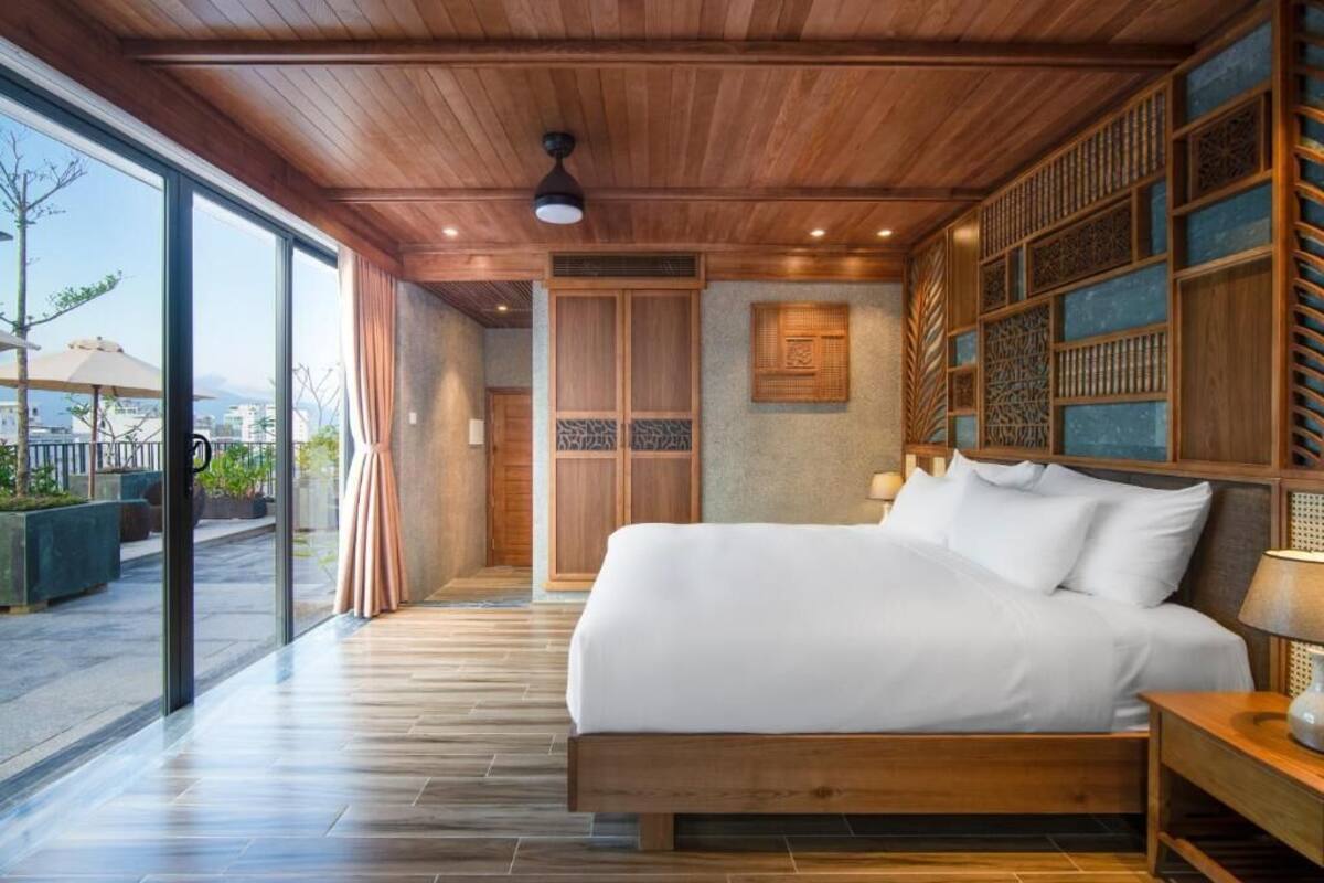 A modern bedroom with a large bed, wooden ceiling, and a view of the outdoors.