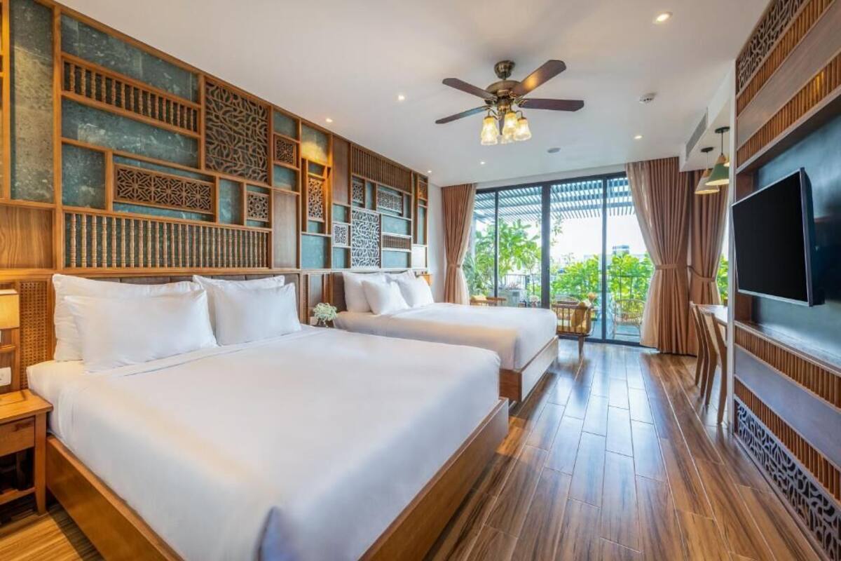 A hotel room with two beds, a ceiling fan, a TV, and a view of greenery outside.