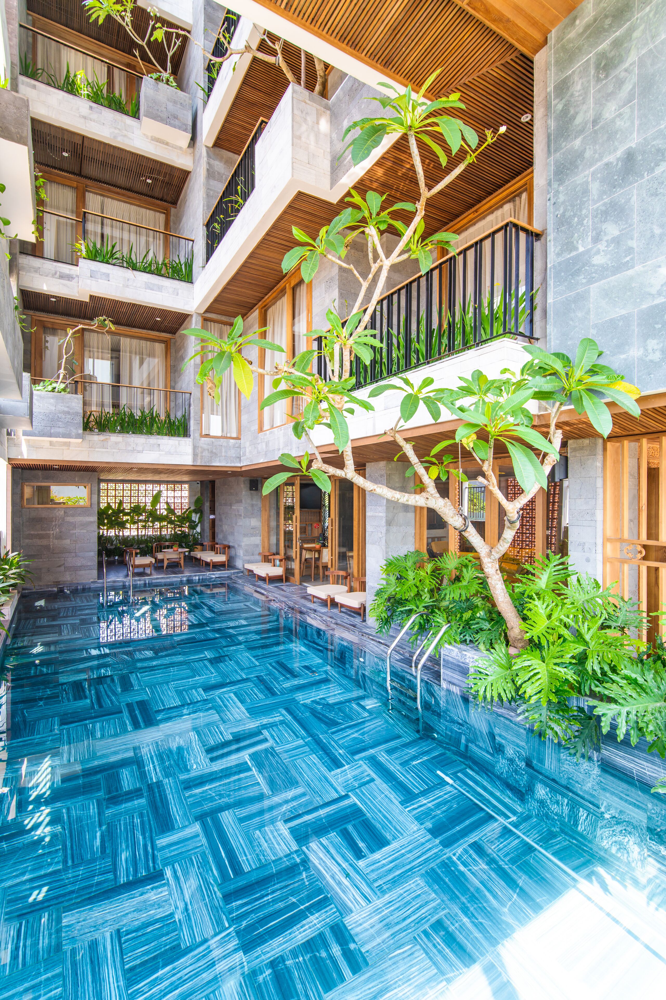 Un espace piscine intérieur à plusieurs niveaux, doté d’un élément aquatique central, entouré d’une végétation luxuriante et d’une architecture moderne.