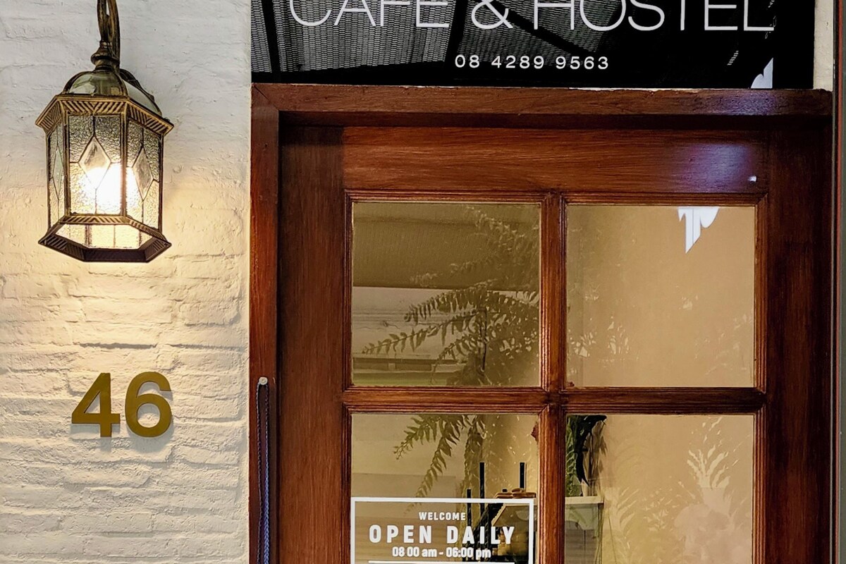 A wooden door with a glass panel, a sign reading "CAFE & HOSTEL" and "OPEN DAILY 08:00 am - 06:00 pm", and a number "46" on the wall.
