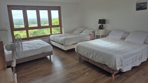A bedroom with two beds, a bedside table with a lamp, and a large window with a view of greenery. - Maison en Pierre Avec Jacuzzi été et Hiver (Perreux)