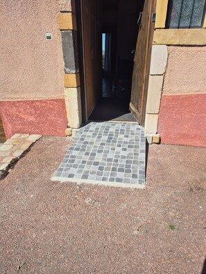A doorway leading to an interior space, with a tiled entrance mat and a stone wall.