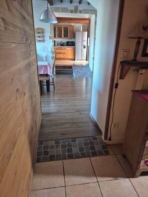 A narrow hallway leading to a kitchen with wooden cabinets, a refrigerator, and a dining area with a table and chairs.
