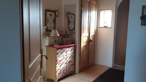 A hallway with a wooden door, a small desk with a lamp, and a tiled floor. - Maison en Pierre Avec Jacuzzi été et Hiver (Perreux)