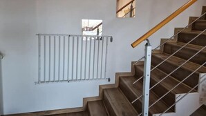 A staircase with wooden steps and a metal handrail, leading to a landing with a white radiator and a small window. - Maison en Pierre Avec Jacuzzi été et Hiver (Perreux)