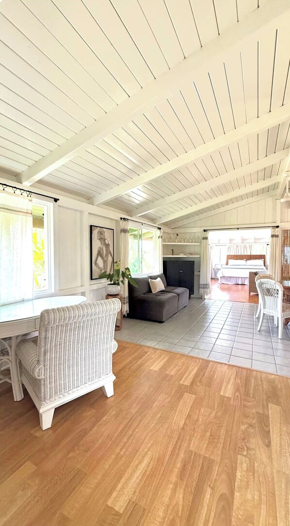 A spacious living area with a high ceiling, a sofa, a wicker chair, and a bed.
