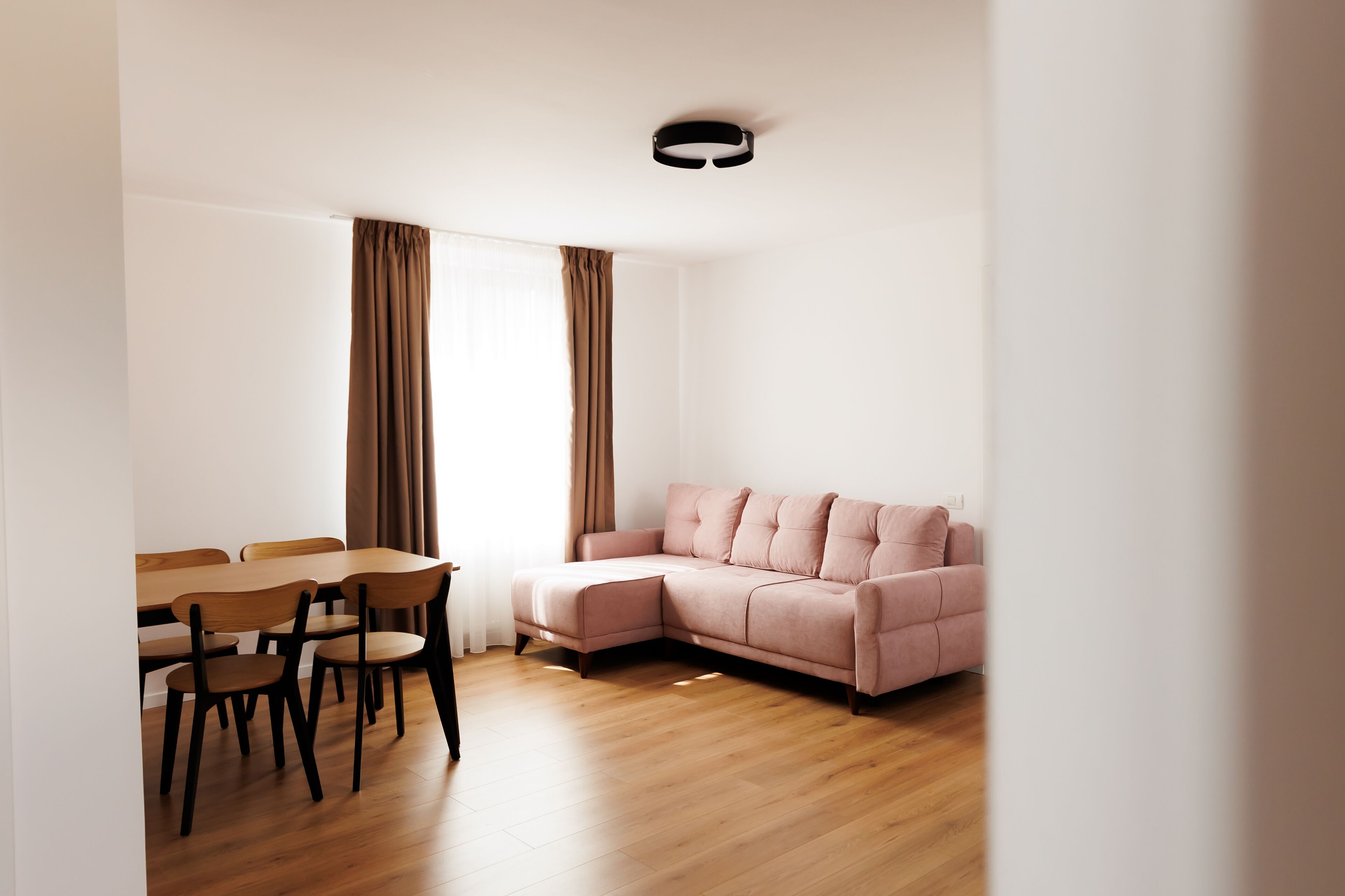 Un soggiorno moderno con un tavolo da pranzo in legno e sedie, un divano modulare rosa e un lampadario.