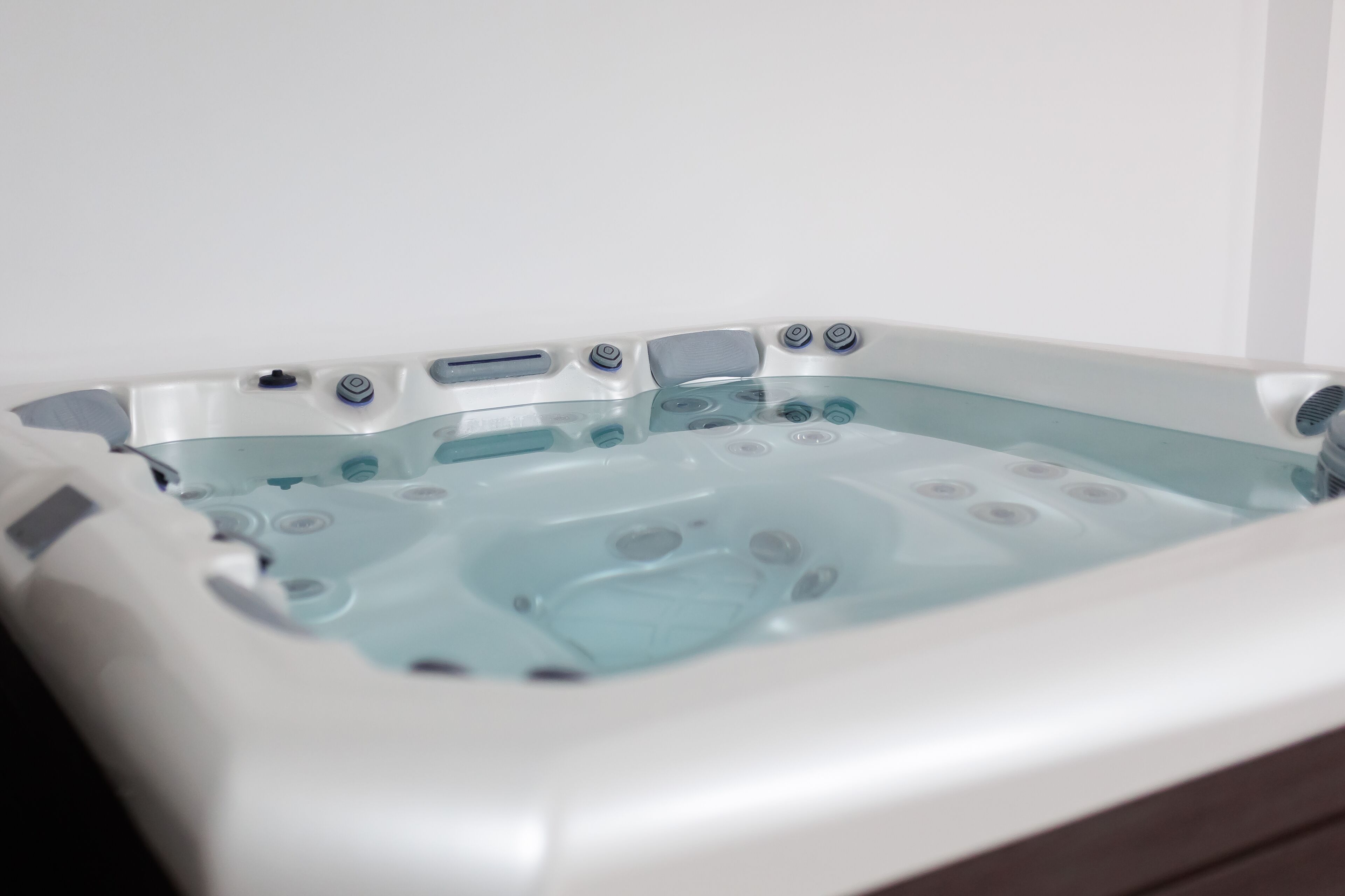A rectangular hot tub with multiple jets, a control panel, and a glass interior.