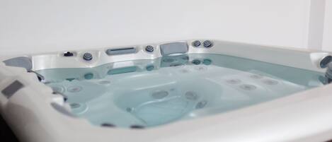 A rectangular hot tub with multiple jets, a control panel, and a glass interior.