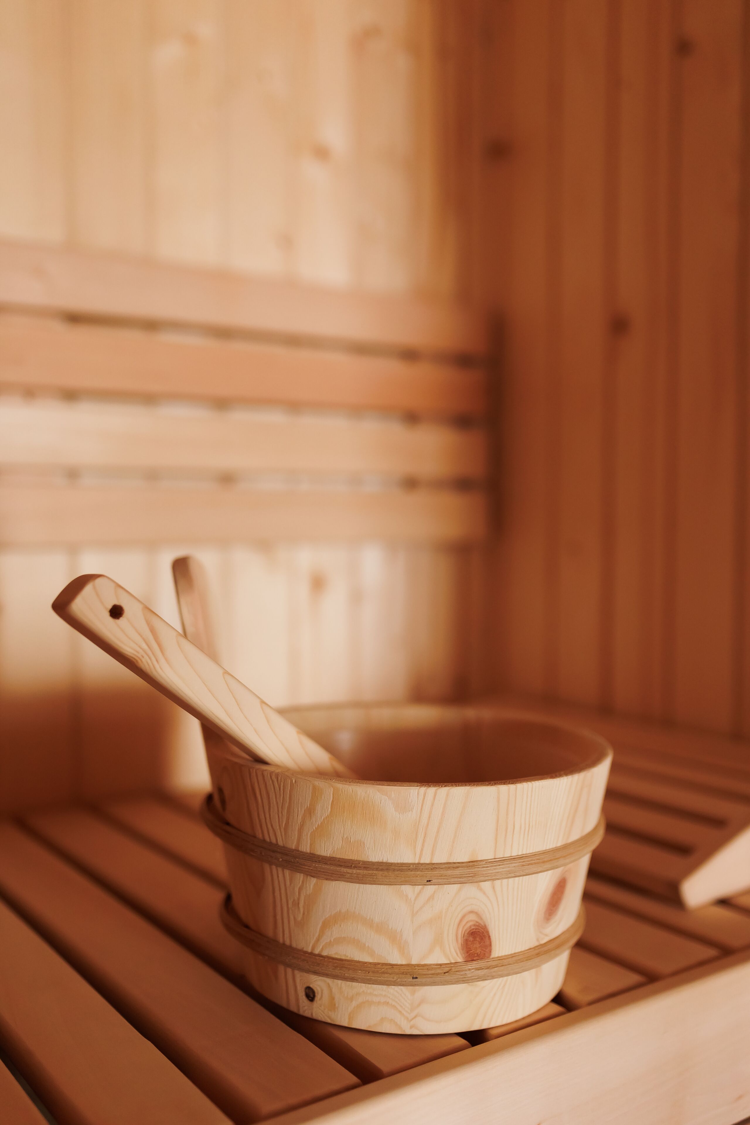 A wooden sauna bench with a wooden bucket containing a wooden spoon.