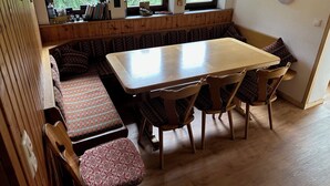 A cozy dining area with a wooden table and benches, large windows with a view of greenery, and a wall with a cross and decorative plates. - Ferienhof Wäldle 2 Balderschwang - Direkt an der Loipe mit Motorradvermietung (Balderschwang)