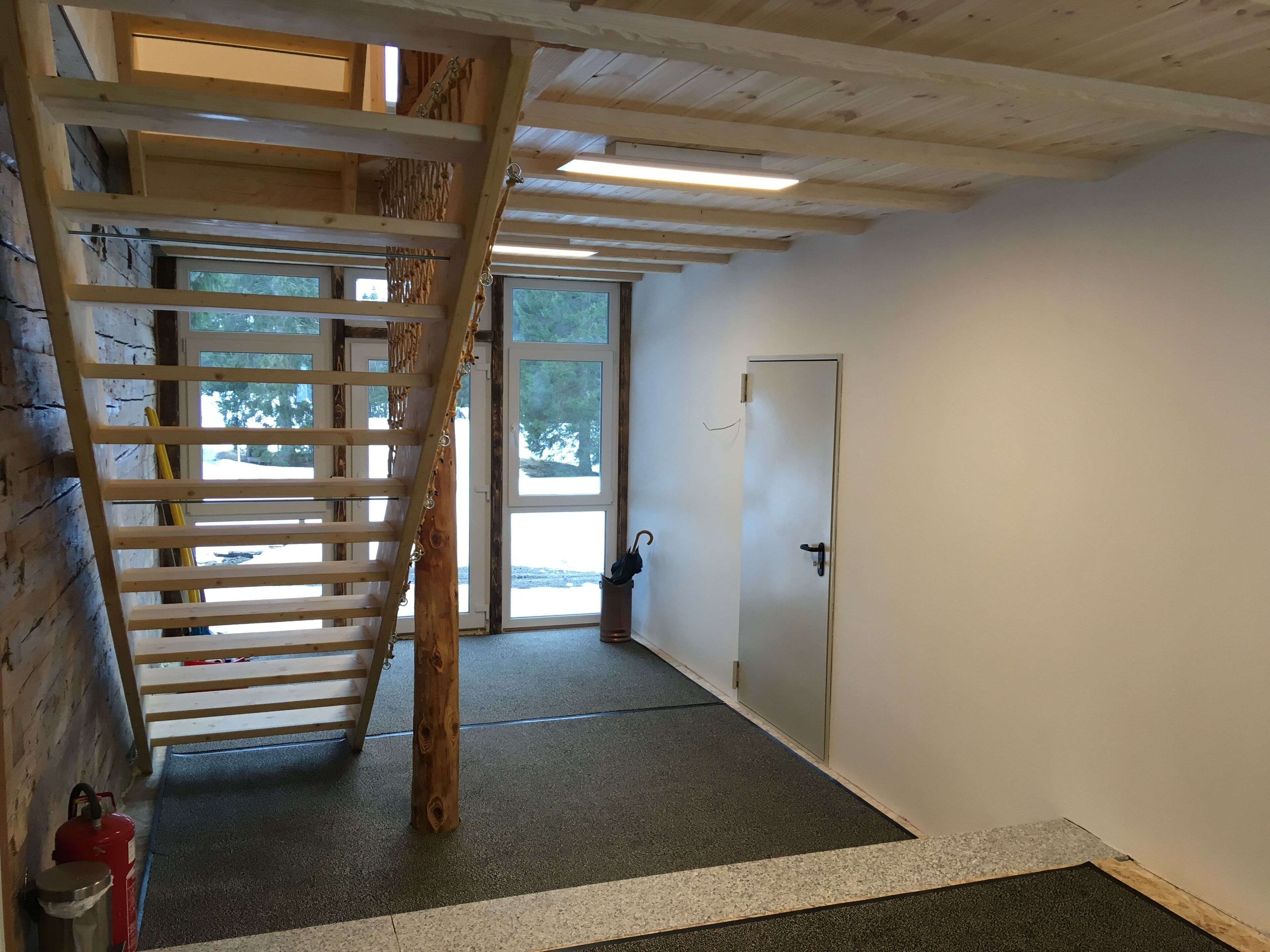 A wooden staircase leading to a second floor, a door, and a fire extinguisher on the floor.