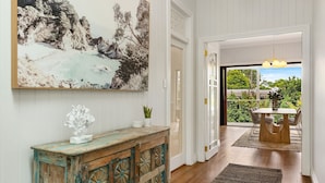 A hallway with a rustic wooden cabinet, a large abstract painting, and a view of an outdoor dining area with a table and chairs.