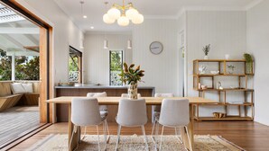 A modern dining area with a wooden table, four grey chairs, a woven rug, and a wooden bookshelf with decorative items.