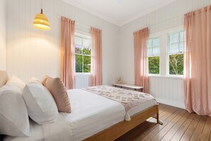 Quarto com cama de madeira, paredes brancas e cortinas cor-de-rosa.