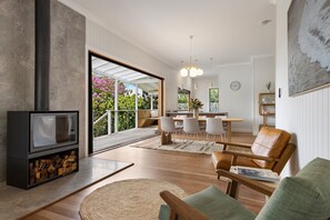 Una sala de estar moderna con chimenea, un comedor con mesa y sillas de madera, y vistas al exterior a través de amplios ventanales.