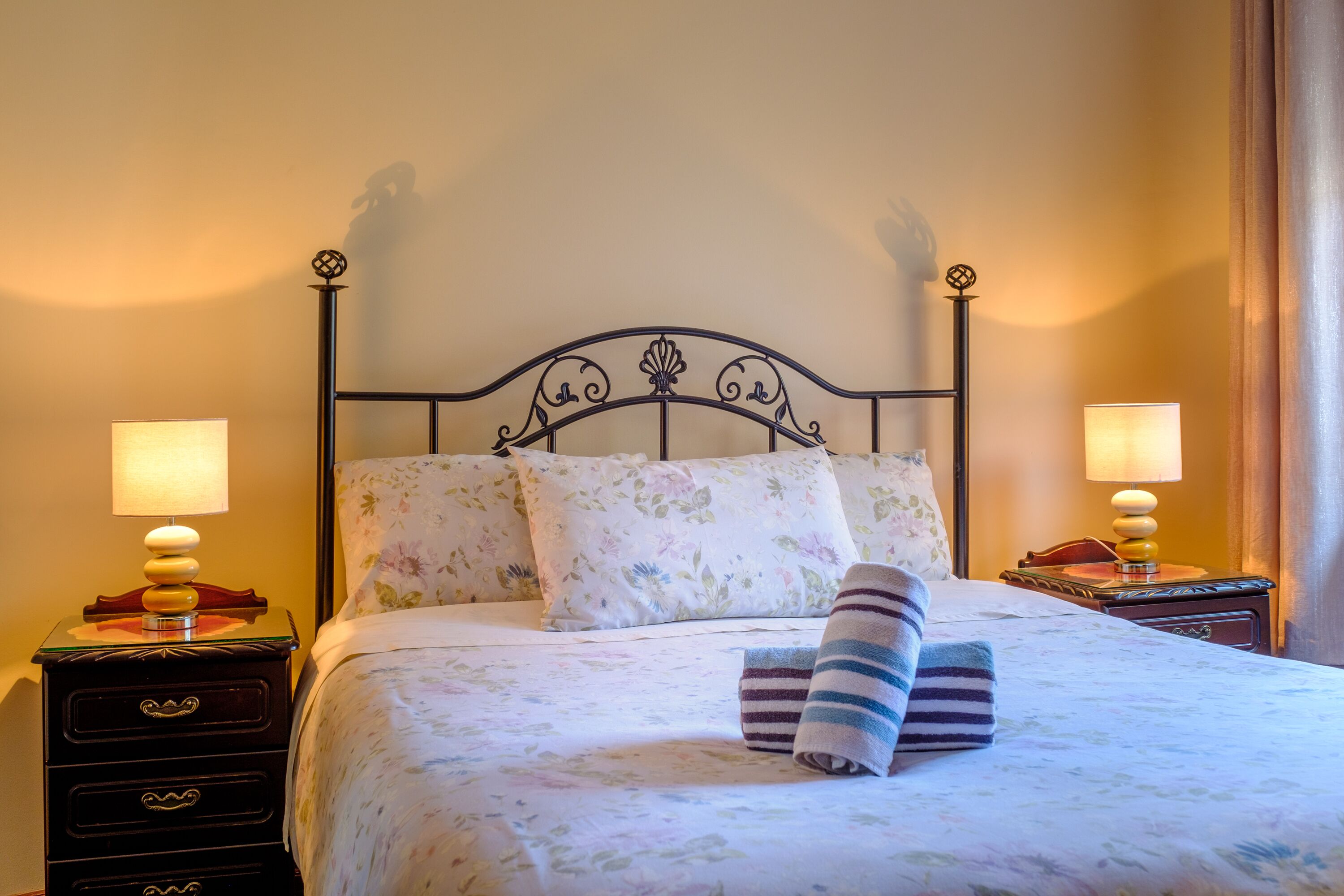 A neatly made bed with floral bedding, two bedside lamps, and a striped towel.