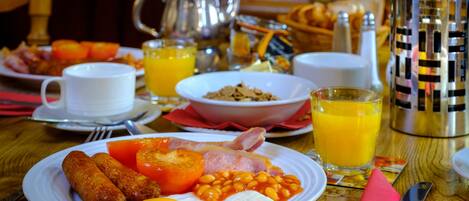 A breakfast table with plates of eggs, bacon, tomatoes, beans, and sausages, along with cups of coffee and orange juice.
