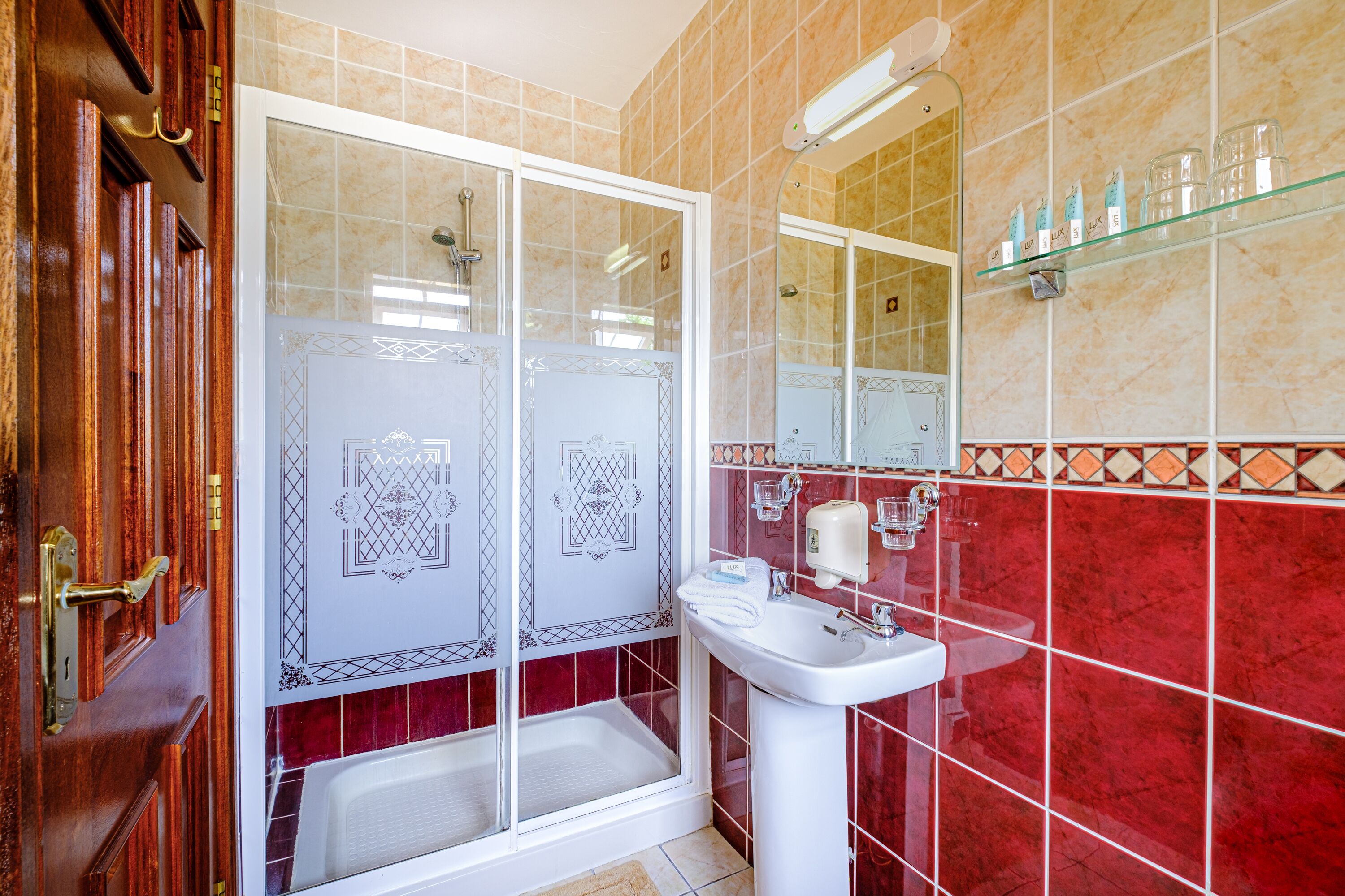 A bathroom with a glass shower enclosure, a sink, and a glass shelf with toiletries.