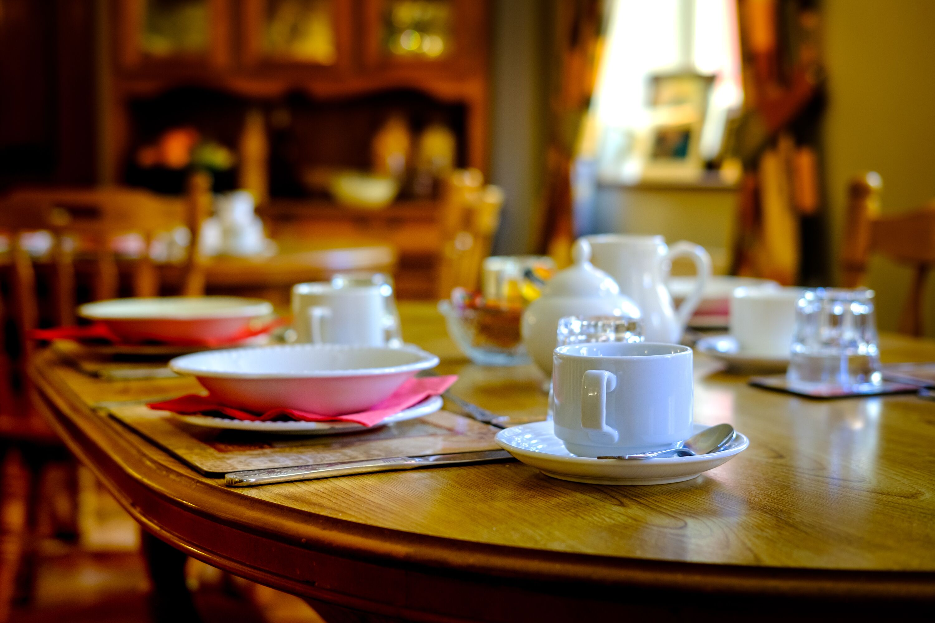 A dining table set with white cups, saucers, and a pink bowl.