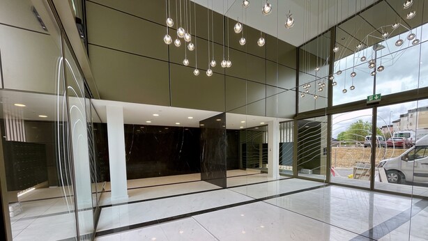 A modern lobby with glass walls, a marble floor, and hanging spherical lights. - Media Bay Apartments (Luxembourg City)