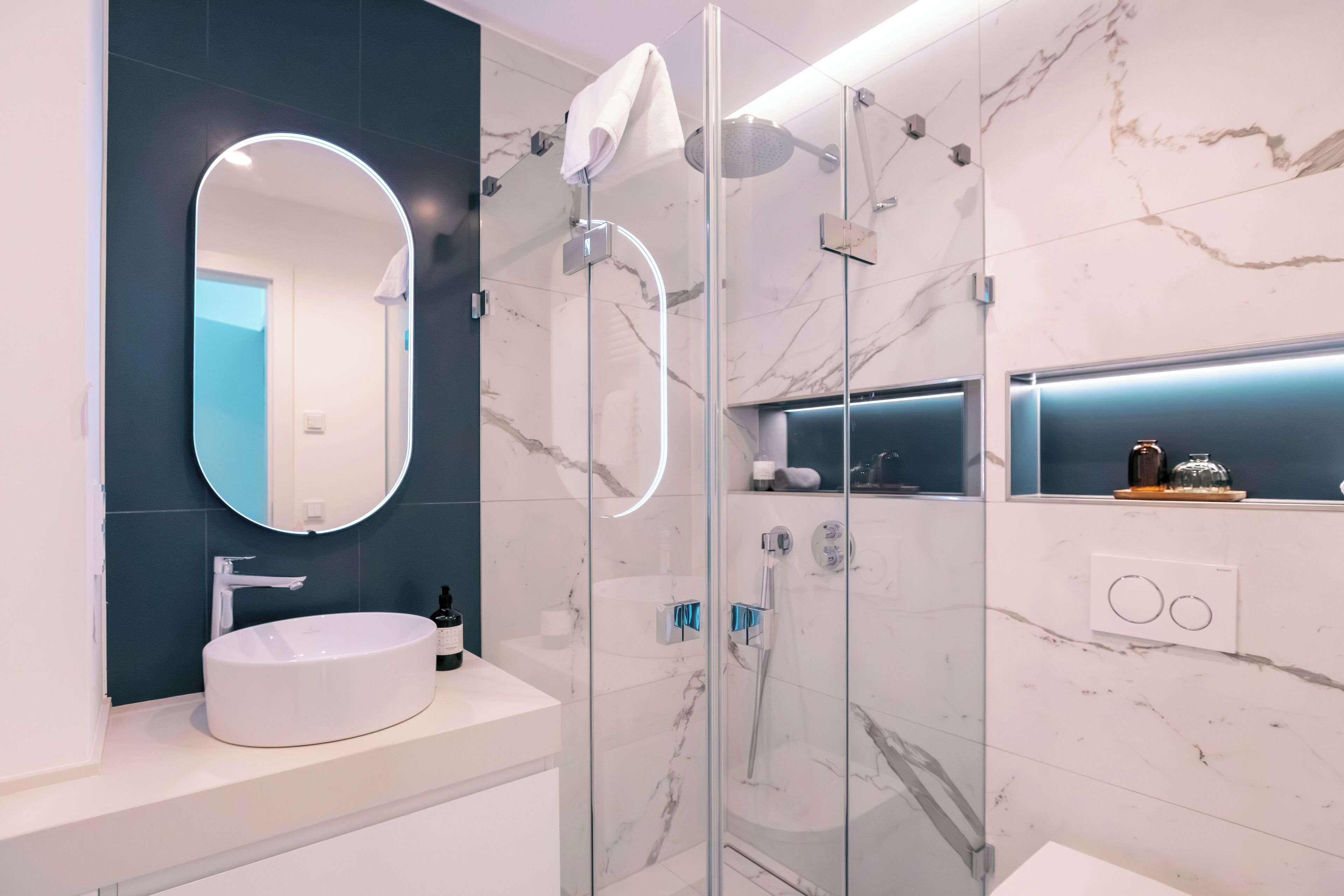 A modern bathroom with a round mirror, a white sink, and a glass-enclosed shower area.