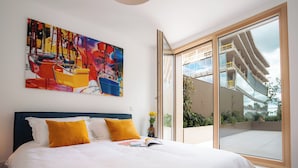 A modern hotel room with a large bed, a colorful abstract painting, and a view of a building through a sliding glass door. - Media Bay Apartments (Luxembourg City)