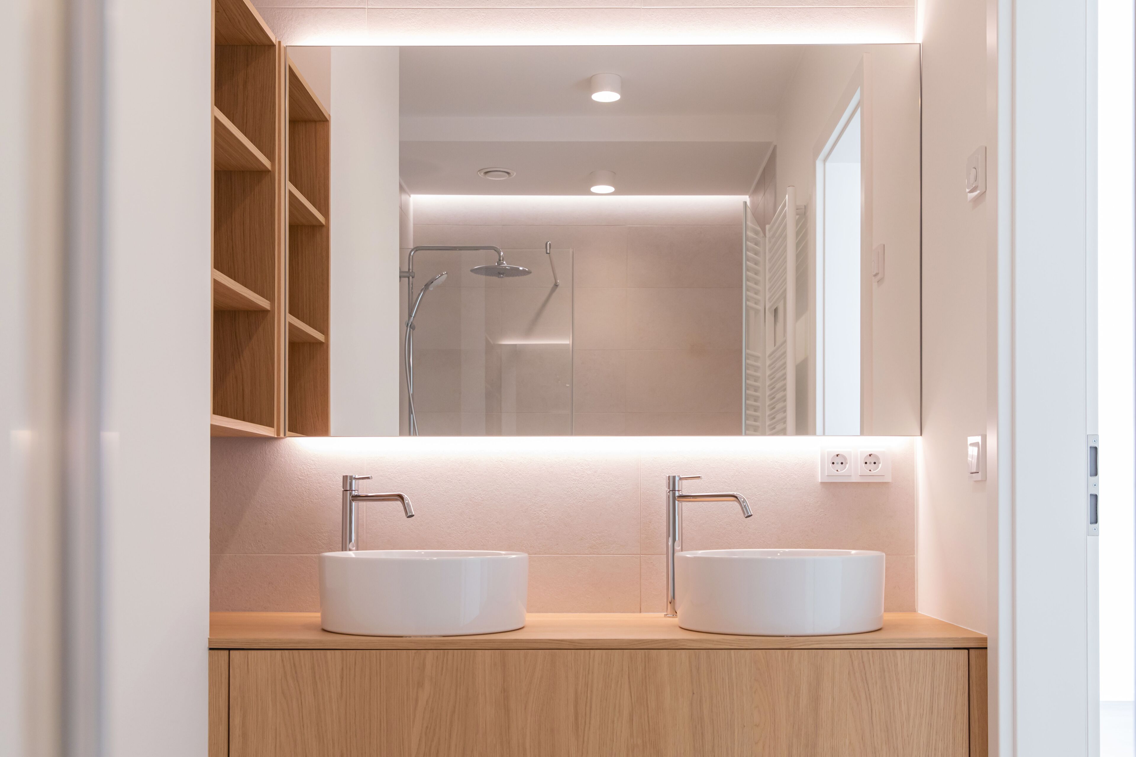 Een moderne badkamer met twee witte wasbakken, een spiegel en een douche.