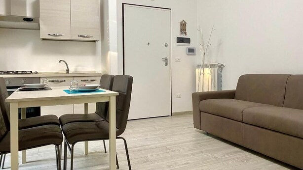 A modern kitchen with a dining table and chairs, a brown sofa, and a white door with a small sign above it. - Casa Brina By Home080 (Monopoli)