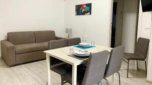 A modern living room with a beige sofa, a dining table with four chairs, and a colorful abstract painting on the wall. - Casa Brina By Home080 (Monopoli)