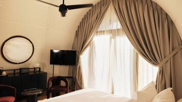 Una habitación de hotel con cama, televisión, escritorio, silla y ventilador de techo.