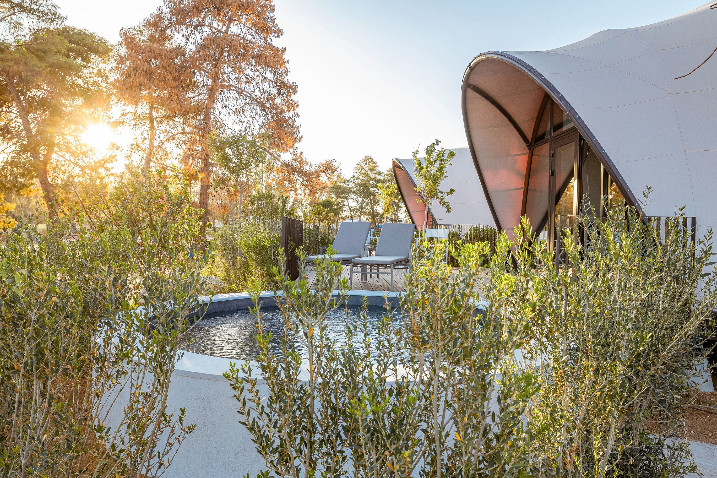 Un área lounge al aire libre y moderna con piscina, rodeada de árboles y una estructura única tipo tienda.